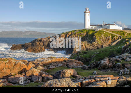 Am späten Abend Sonne auf den Leuchtturm und Lough Swilly im Hintergrund als weiße Wellen gegen die Felsen unten Fanad Head County Donegal Irland. Stockfoto