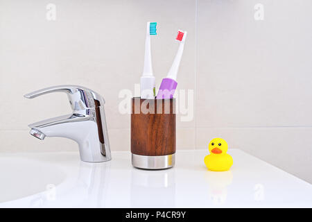 Zwei elektrische Zahnbürsten in Holz Glas am Waschbecken im Badezimmer gelb Ducky Duck. Persönliche Hygiene Konzept. Stockfoto