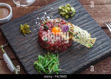 Beef Tartar mit Kapern, Gurken und frischen Zwiebeln auf dunklem Hintergrund Stockfoto