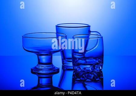 Transparente Glas Gläser stehen auf einer glänzenden Oberfläche auf einem blauen Hintergrund Stockfoto