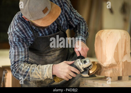 Сarpenter in Arbeitskleidung und kleine Steuerungsfunktionen für Eigentümer in Holzarbeiten Workshop, Prozesse der Vorstand mit einem Winkelschleifer, auf dem Tisch ist ein Hammer ein Stockfoto