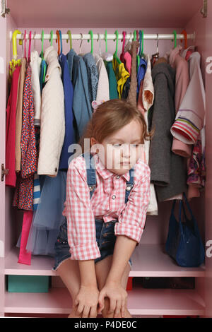 Ein kleines Mädchen sitzt in einem Schrank mit einer Abteilung. Storage System für Sachen für Kinder Stockfoto