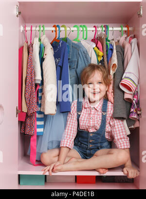 Ein kleines Mädchen sitzt in einem Schrank mit einer Abteilung. Storage System für Sachen für Kinder Stockfoto