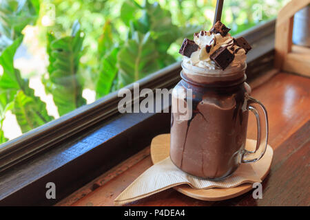 Dunkle Schokolade Milchshake mit Schlagsahne brownie auf Holz Tisch, Fenster Cafe Hintergrund, trinken Sommer. Stockfoto