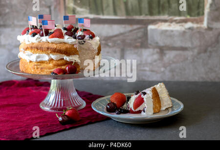 Patriotische angelfood Kuchen mit Rot weißen und blauen Beeren und amerikanische Flaggen, und eine Scheibe bereit zu essen Stockfoto