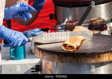 Die Landwirte Creperie, Landwirte Street Food Markt, Anbieter führt wie Pfannkuchen, Crepes zu machen. Chef's Hände in blaue Handschuhe Schnitt der gerollte Pfannkuchen auf der Stockfoto