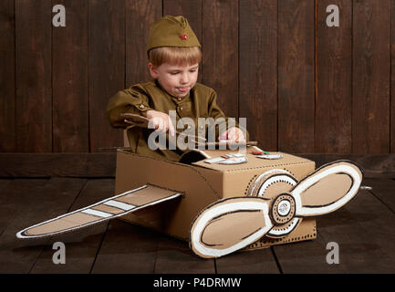 Kinder Jungen sind als Soldat in retro militärische Uniformen Reparatur ein Flugzeug von Karton, dunklen Hintergrund, retro style Stockfoto