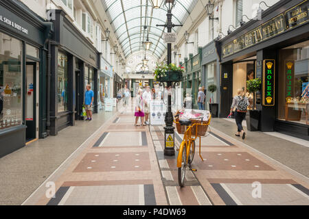 Käufer und ein gelbes Fahrrad in der Arcade, Bournemouth, Dorset, Großbritannien Stockfoto