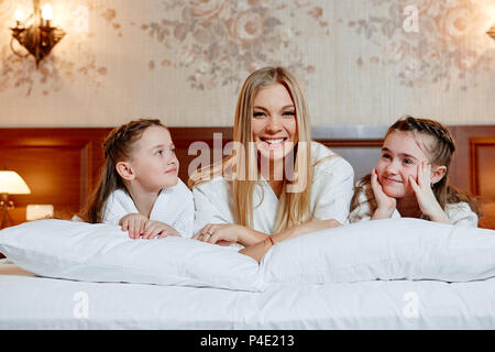 Porträt einer Lachen Mutter und ihre zwei Kinder liegen auf einem Bett in einem gemütlichen Zimmer. Stockfoto