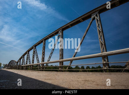 Altes rostiges Metall Geländer auf der Brücke über den Fluss an einem sonnigen Tag. Straße mit Risse im Asphalt Stockfoto