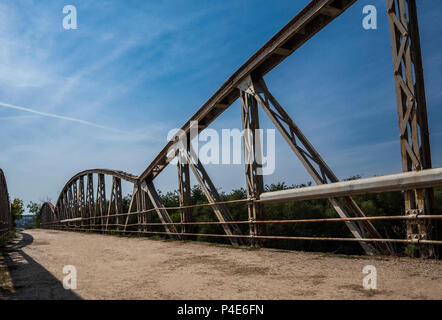 Straße mit Risse im Asphalt an der Brücke über den Fluss an warmen sonnigen Tag. Altes rostiges Metall Geländer Stockfoto