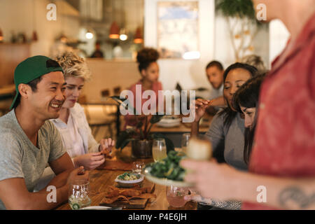 Lächelnden jungen Freunden vergnügen, während in einem Bistro sitzen Stockfoto