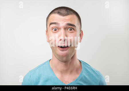 Überrascht junger Mann in Polo-T-Shirt über grauen Hintergrund. Close up Portrait von positive Facial emotion Stockfoto