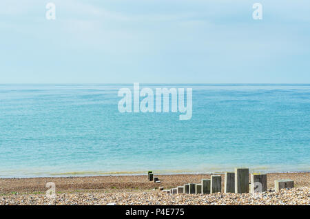 Pebble Beach Szene von ruhigen Meer am hellen Tag. Holz- beiträge in unterschiedlichen Höhen führen, in Richtung der Küste. Stockfoto