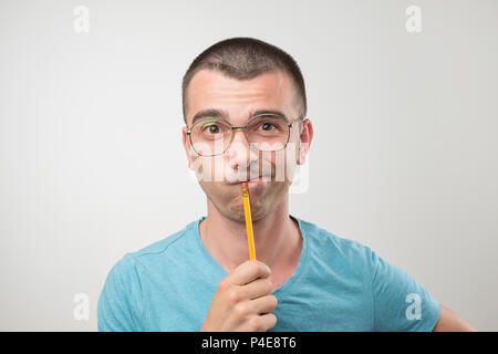 Junger Mann im blauen Hemd haben eine Idee. Er setzt Bleistift auf den Mund. Denken oder Pläne Stockfoto