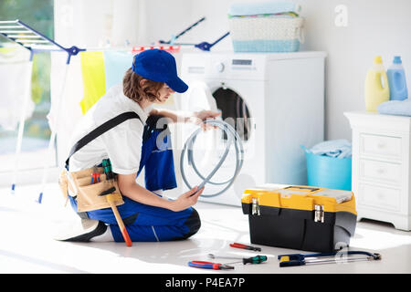 Waschmaschine Reparatur Service. Junge männliche Techniker in der blauen Uniform untersuchen und reparieren defekte Waschmaschine oder Trockner. Wartung von Home und h Stockfoto