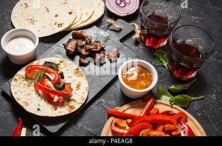 Frische und köstliche mexikanische Tacos und Lebensmittelzutaten, die in schwarzen Stein Hintergrund. Das Kochen. Ansicht von oben Stockfoto