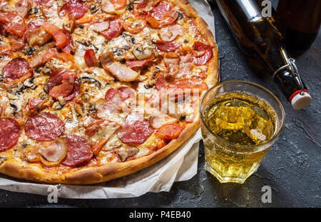 Frische, hausgemachte Pizza mit Salami, Schinken, Käse und ein Glas Bier auf rustikalem Stein Hintergrund. Stockfoto