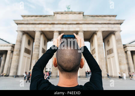 Nahaufnahme eines jungen kaukasischen Mann, von hinten gesehen, ein Bild von der beliebten Brandenburger Tor in Berlin, Deutschland, mit seinem Smartphone Stockfoto