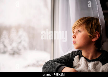 Junge Blick aus dem Fenster im Winter Stockfoto