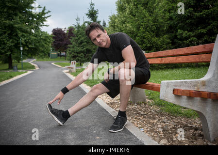 Mann sitzt auf einer Bank, Stretching, bevor er ausgeführt wird Stockfoto