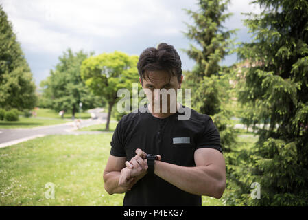 Man Standing in Park schaut auf seine Uhr, während der Ausübung Stockfoto