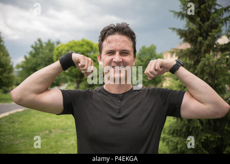 Lächelnder Mann, der Park seine Muskeln Stockfoto