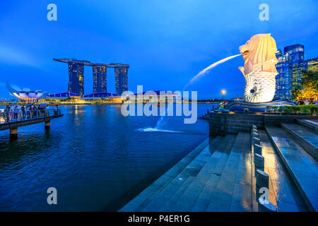Singapur - 27. April 2018: Die Statue Singapur Merlion in der Marina Bay. Merlion hat Kopf und ein Löwe Fische Körper und das Herausspritzen von Wasser aus seinem Maul. Marina Bay Sands Türme in der Skyline. Stockfoto