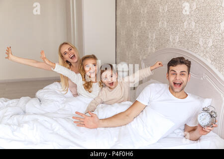 Glückliche junge Familie Aufwachen zusammen mit Wecker Stockfoto