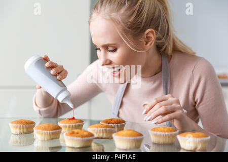 Schönen lächelnden jungen Frau im Vorfeld vorbereiten leckere Muffins mit Marmelade Stockfoto