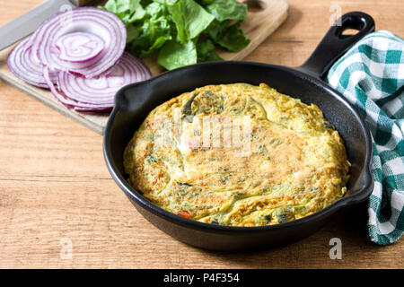 Frittata aus Eier und Gemüse in eine eiserne Pfanne, auf hölzernen Tisch. Stockfoto