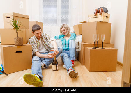 Foto von Mann mit einer Flasche Wein und Frau sitzt auf einem Sofa unter Kartons Stockfoto