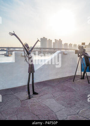 Metall Skulpturen auf der Haeundae promenade Förderung der Busan International Film Festival mit dem gwangan Bridge im Hintergrund bei Sonnenuntergang, Bu Stockfoto