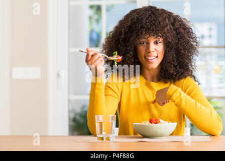 Afrikanische amerikanische Frau essen Pasta Salat zu Hause mit Überraschung Gesicht zeigenden Finger zu sich selbst Stockfoto