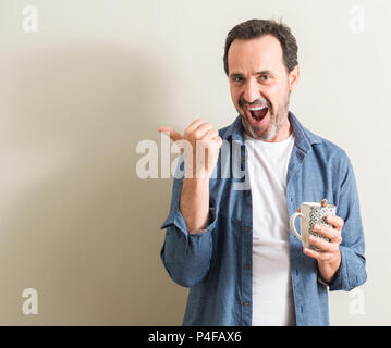 Ältere Menschen trinken Kaffee in einem Becher zeigt mit Finger- und oben mit glücklichen Gesicht lächelnd Stockfoto