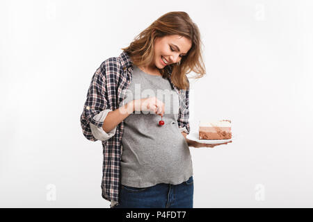 Lächelnd schwangere Frau Halteplatte mit Kuchen und Cherry ordentlich Bauch auf weißen isoliert Stockfoto