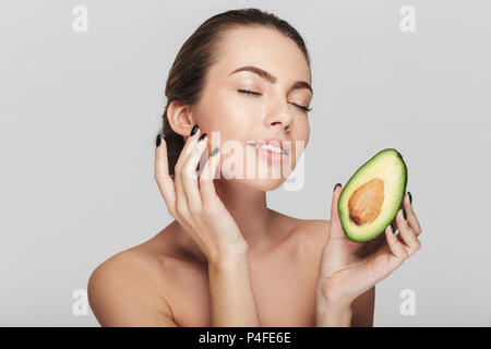 Junge Frau mit perfekter Haut halten die Hälfte der frischen Avocado isoliert auf weißem Stockfoto