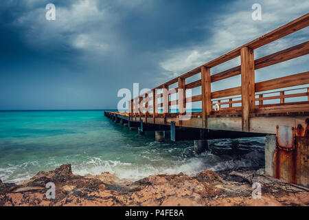 Blick auf die hölzerne Seebrücke von der türkisfarbenes Meer mit dramatischen Dunkelblaue Wolken. Stockfoto