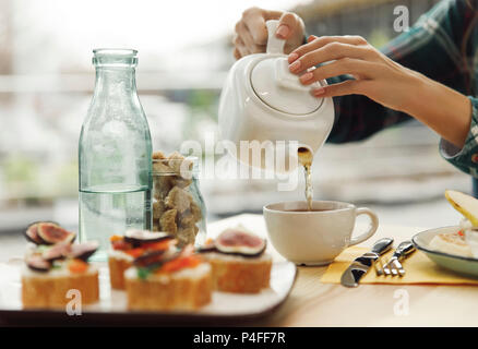 Schuß von Mädchen gießt Tee von Teekanne in Tasse zum Frühstück 7/8 Stockfoto