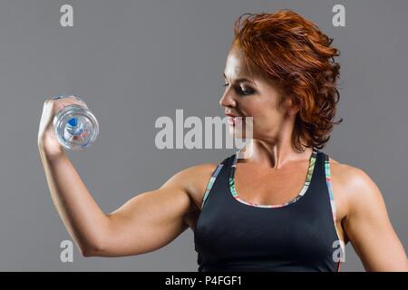 Nach athletic Fitness rothaarige Frau in Sport Uniform mit einer Flasche Wasser, grauen Hintergrund. Stockfoto