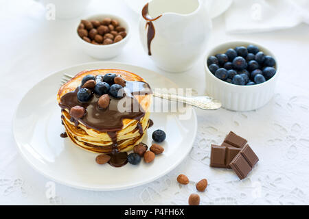 Das traditionelle Frühstück Konzept. Stapel Pfannkuchen mit Schokoladensauce, Blaubeeren und die Muttern an der weißen Tischdecke. Selektiver Fokus Stockfoto
