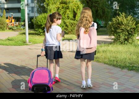 Ansicht der Rückseite zwei Schulmädchen Freundinnen Grundschüler gehen mit Schultasche auf dem Hof. Stockfoto