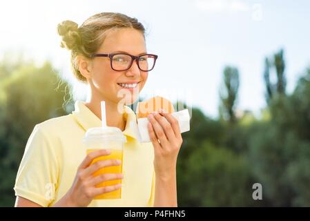 Nett lächelnden Teenager in Schuluniform Holding einen Hamburger und Orangensaft. Zurück zur Schule Stockfoto