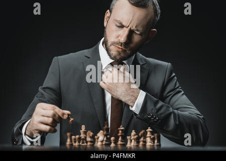Portrait der kaukasischen Geschäftsmann Schach spielen am Tisch isoliert auf Schwarz Stockfoto