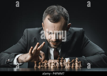 Portrait von konzentrierte Geschäftsmann Schach spielen am Tisch isoliert auf Schwarz Stockfoto