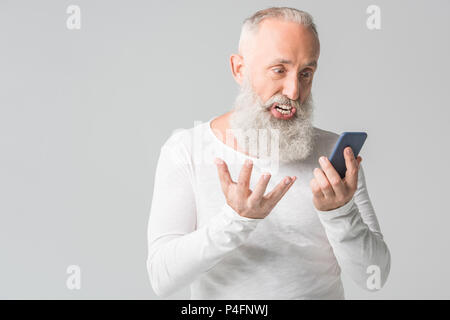 Wütend älterer bärtiger Mann mit Smartphone, isoliert auf weißem Stockfoto