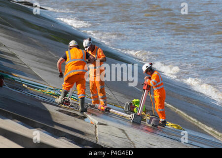 Drei Arbeiter, die Kleidung mit hoher Sichtbarkeit tragen, die sich um die Defekte der Meeresverteidigung kümmert; Balfour Beatty übernimmt die Reparatur der Ufermauer an der Wellenreflexionsmauer in Thorton Cleveleys. Ingenieure einer Baufirma, die von lokalen Räten beschuldigt wird, das vierjährige Programm in Blackpool zu verpfuschen, das 27,1 Mio. £kostete, nachdem sich zwischen den Abschnitten der Betonmeerwand aufgrund von Wasserschäden und Paneelen, die Erosionszeichen zeigten, Lücken gebildet hatten. Balfour Beatty sagte, es sei bekannt, dass Wasser aus einem Gelenk zwischen Betonabschnitten in Richtung des nördlichen Endes des Anchorsholme-Hochwasserschutzes austritt. Stockfoto