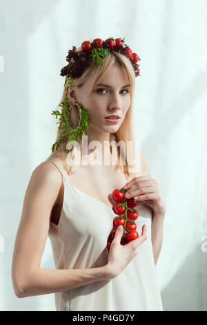 Junge Frau mit Cherry Tomaten in den Händen und Ohrring aus frischen Rucola, vegane Lebensweise Konzept Stockfoto