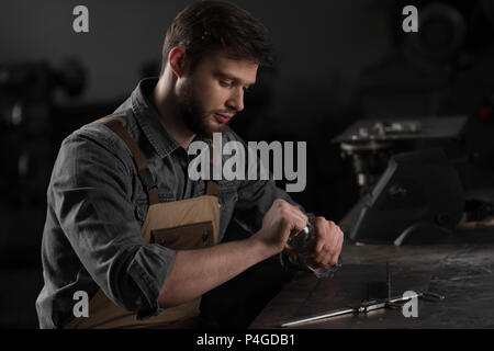 Junge männliche Arbeitnehmer öffnen Flasche Wasser und Sitzen am Tisch Stockfoto