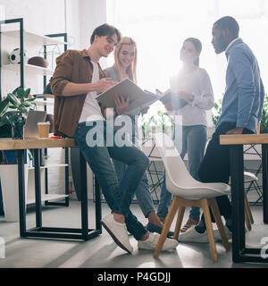 Lächelnd multiethnischen Geschäftsleute und Lehrbücher in Diskussion in modernen Büro Stockfoto